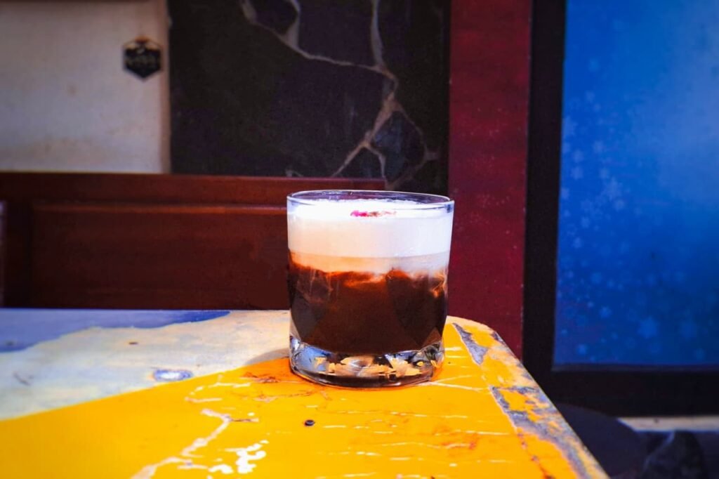 Segelas kopi dengan foam manis di atasnya dihidangkan di meja