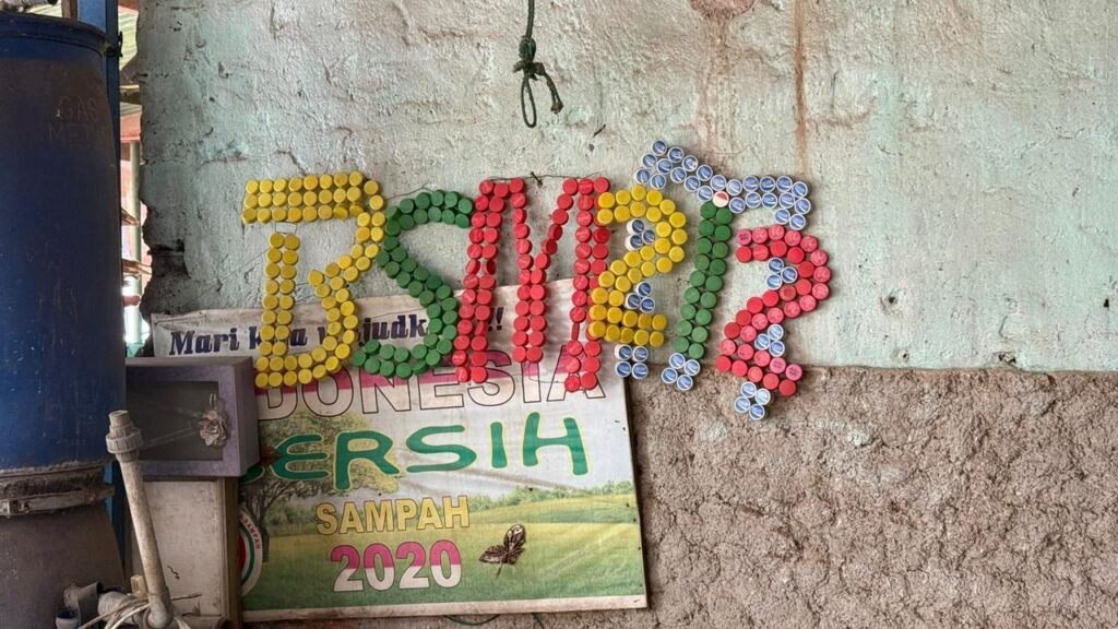 Logo BSM M212 tersusun dari tutup botol plastik warna-warni di dinding galeri daur ulang.