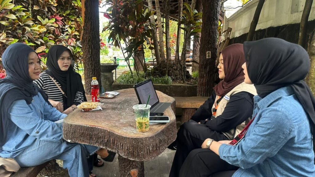 Empat mahasiswa duduk mengelilingi meja di area terbuka sambil melakukan wawancara dan mencatat informasi terkait pengembangan alat steam press ecoprint.
